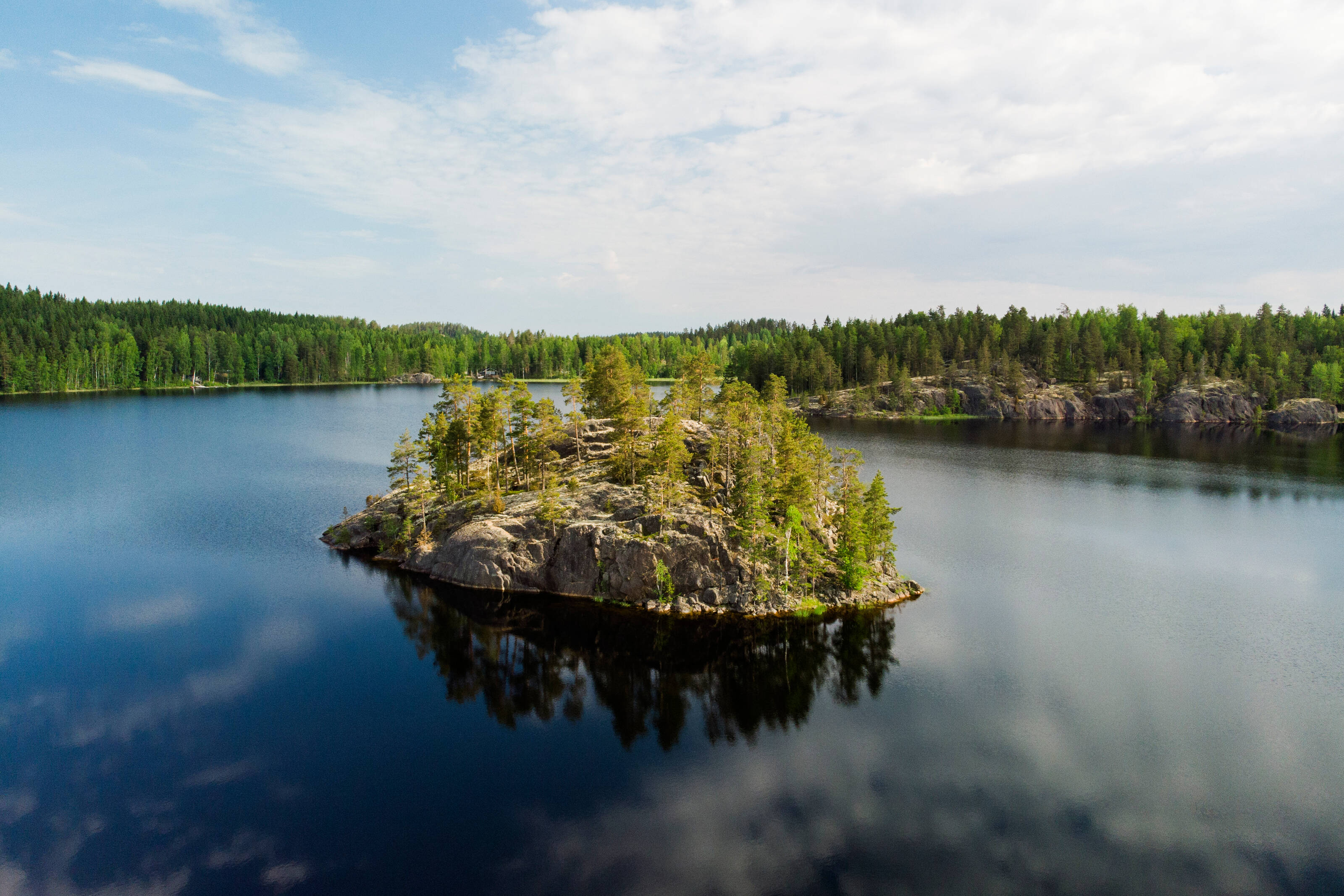 Yläviistosta otettu kuva kallioisesta saaresta keskellä järveä puolipilvisenä kesäpäivänä.