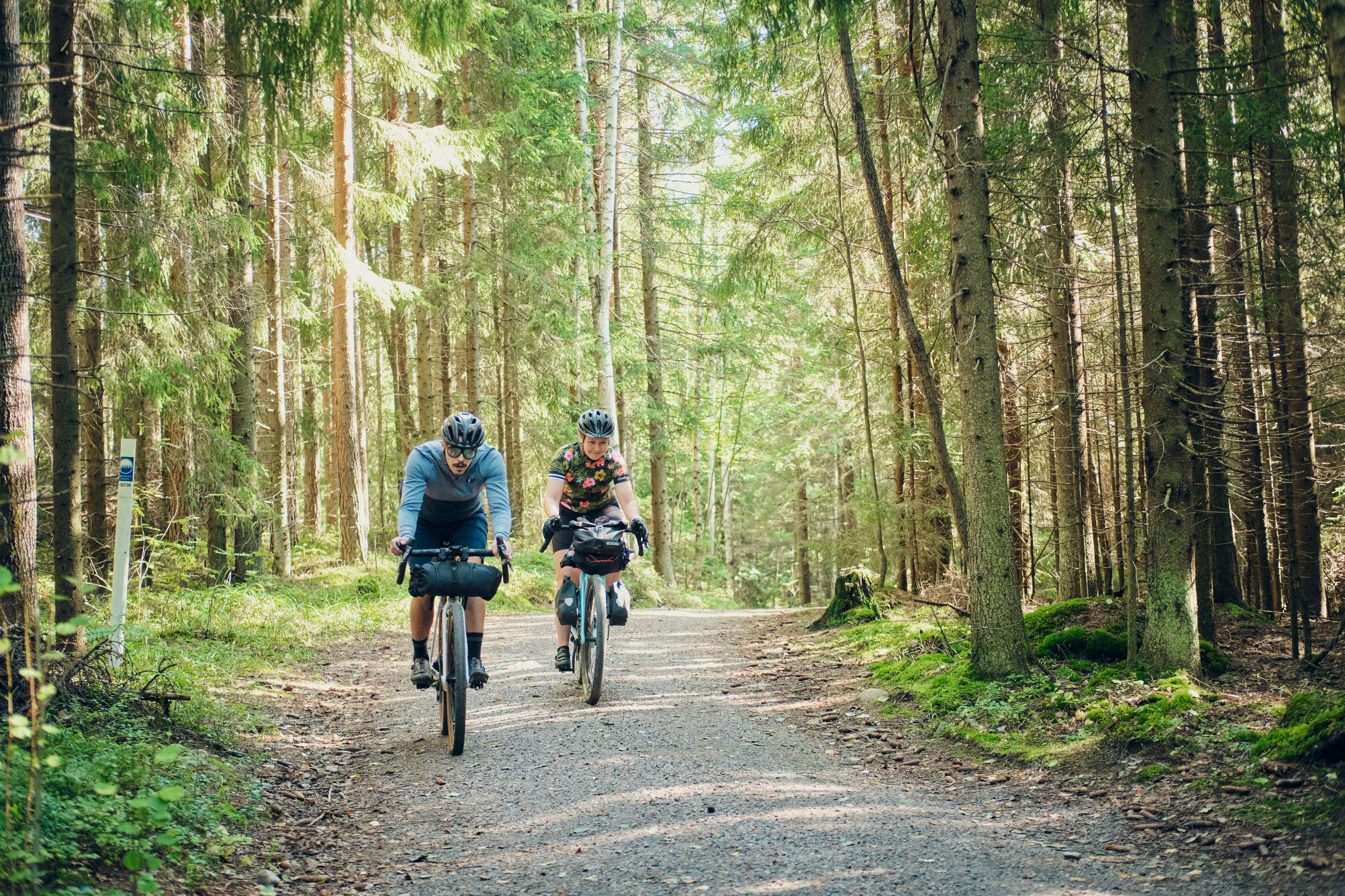 Kaksi pyöräilijää metsässä hiekkatiellä