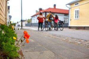 Kolme pyöräilijää taluttaa polkupyöriään vanhankaupungin kadulla.