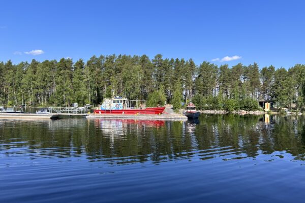 Venesatama vesiltä, laiturissa suuri punainen pyörälautta Rasti. Taustalla mäntypuustoa.
