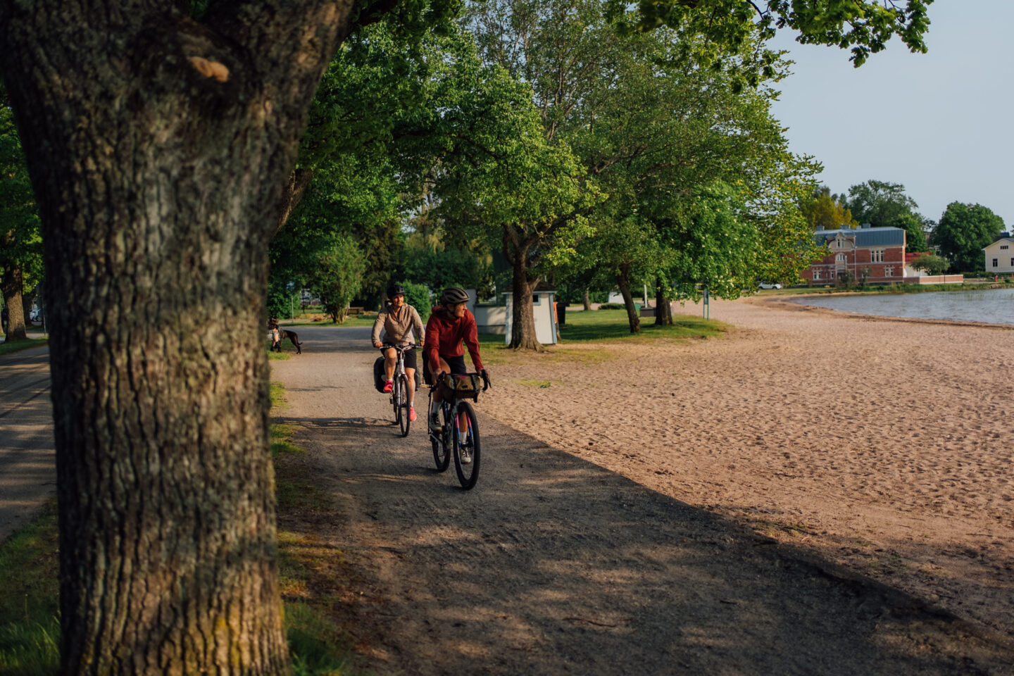 Two cyclists riding a gravel road next to a beach during a sunrise