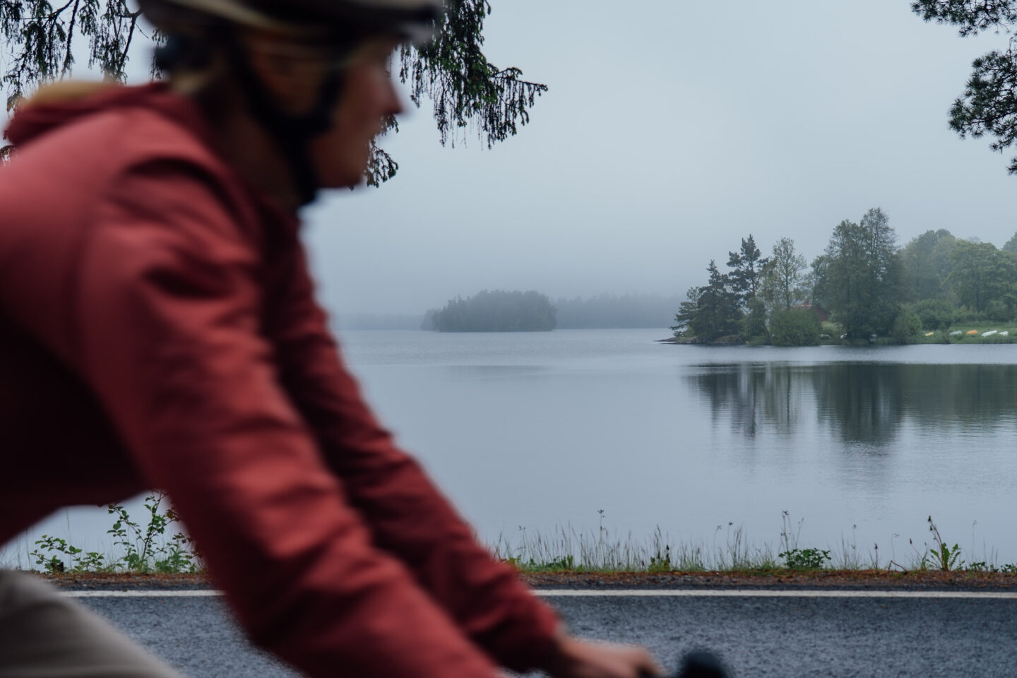 A close-up picture of a cyclist riding a paved road next to waterfront on a rainy day