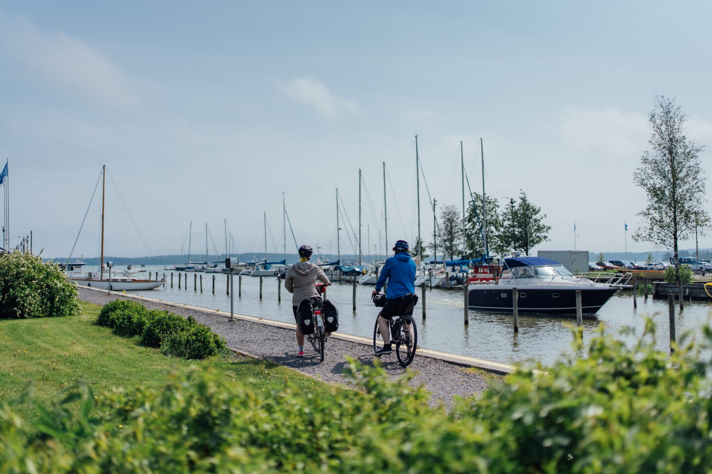 Two cyclists standing with their bikes and watching boats in a harbor