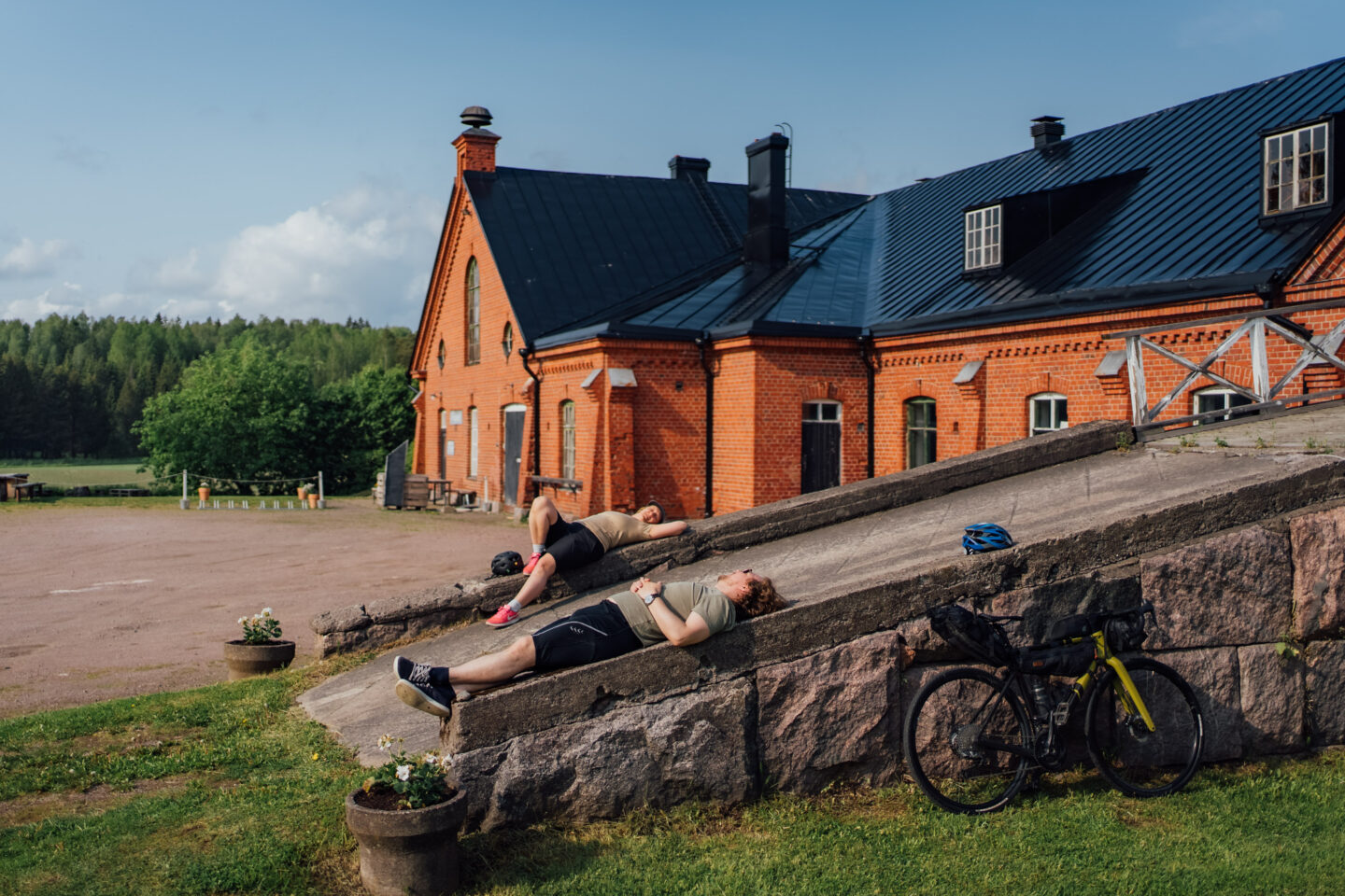 Two cyclists laying on a ramp in front of a big red country mansion