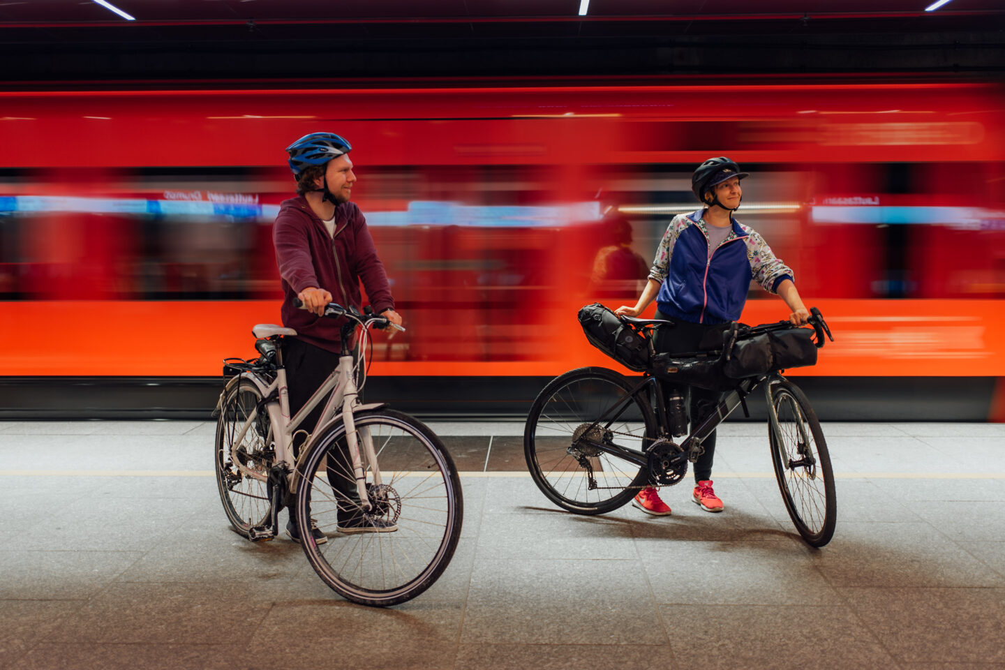 Two cyclists standing with their bikes waiting for a metro on the station