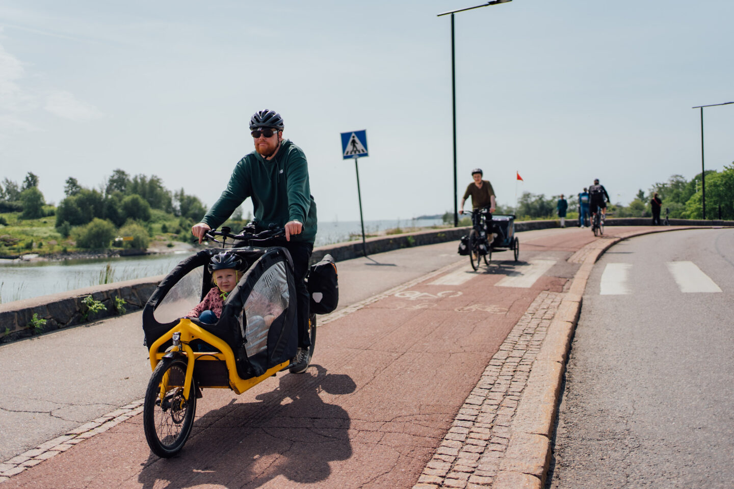 Parents riding with children in a cargo bike and a baby trailer, on a bike path next to the seaside