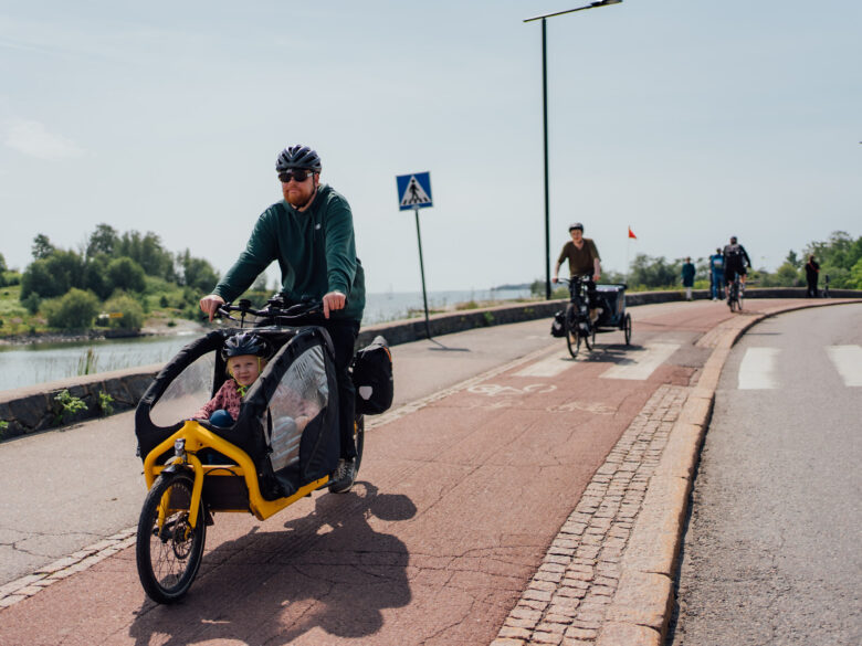 Parents riding with children in a cargo bike and a baby trailer, on a bike path next to the seaside
