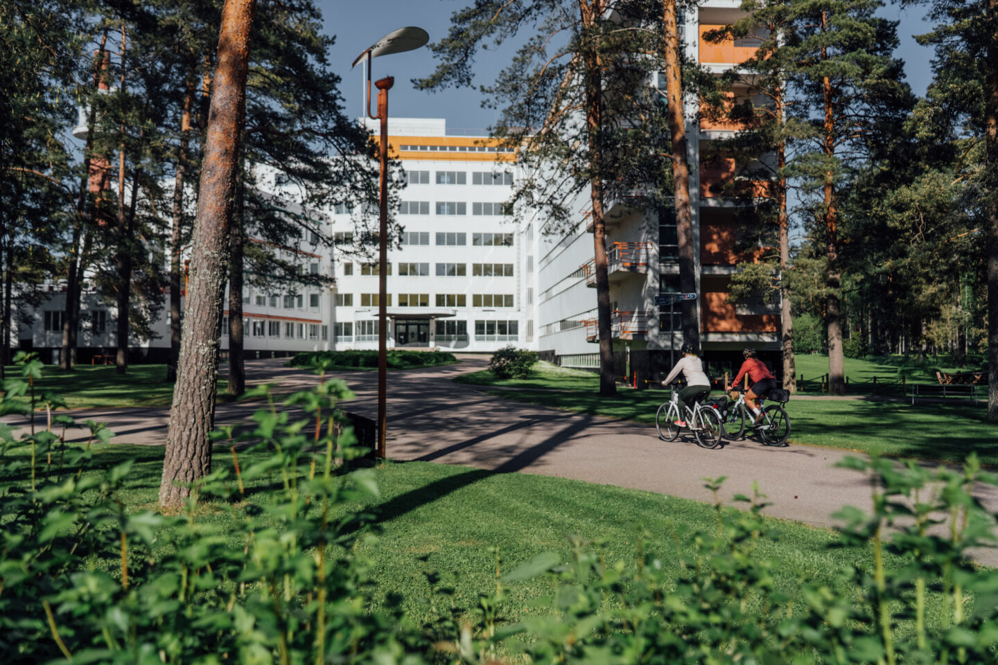 Two cyclists riding a gravel road leading to a big building