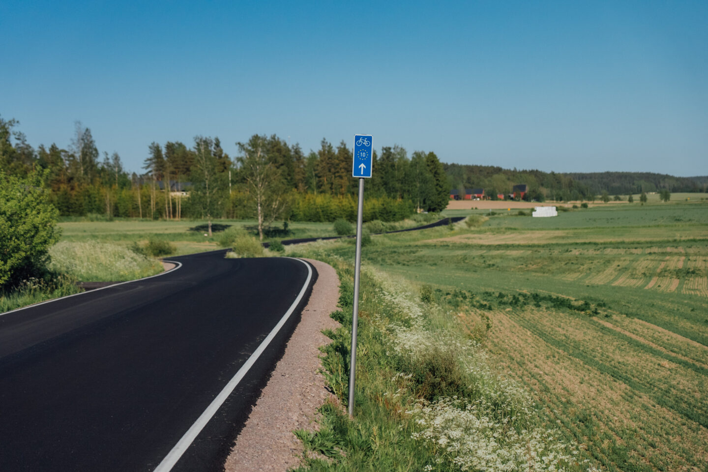 A EuroVelo 10 signpost next to a freshly paved road going through fields