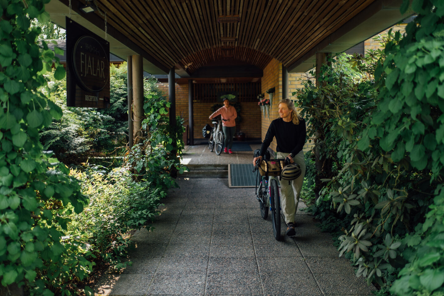 Two cyclists walking their bikes out of the accommodation through a garden