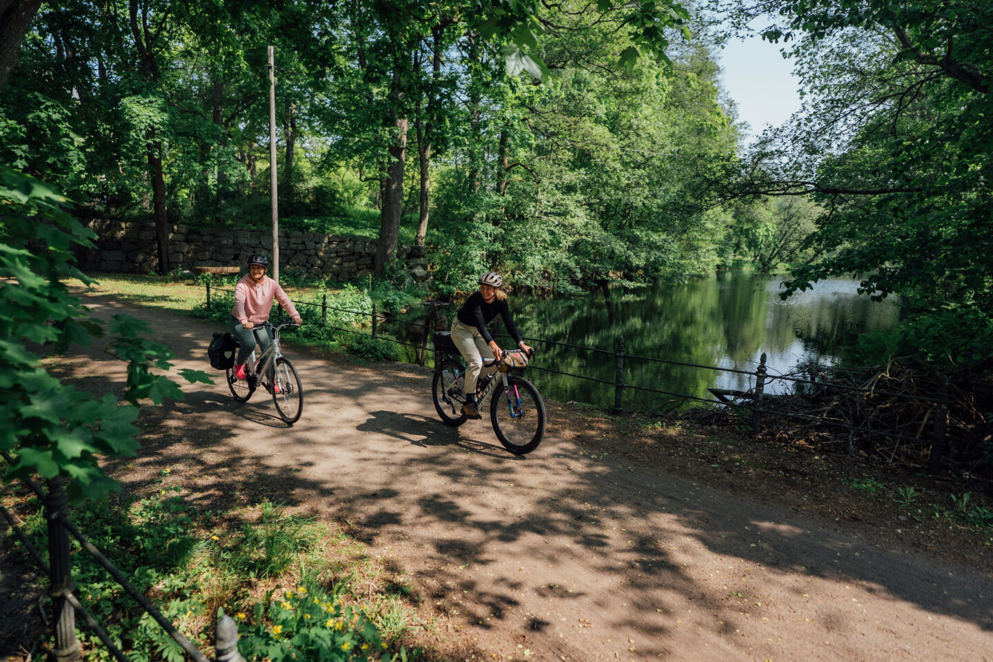 Two cyclists riding a gravel road over a river in a forest park