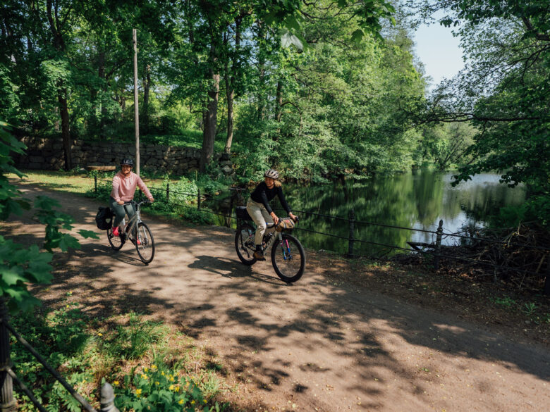 Two cyclists riding a gravel road over a river in a forest park