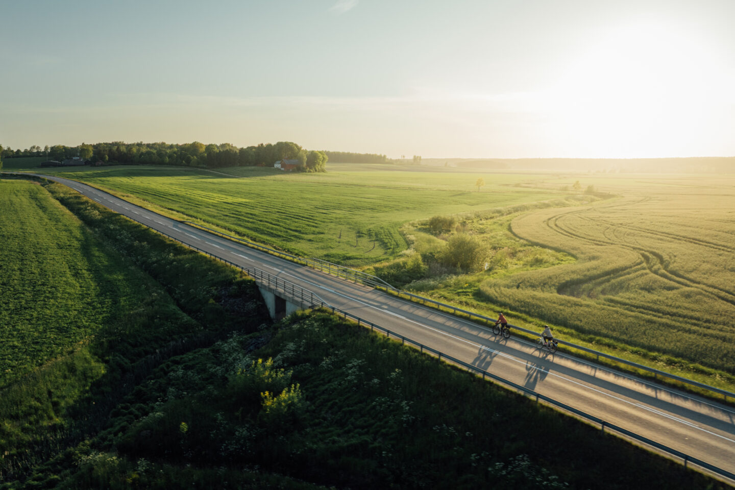 An air picture of two cyclists riding a paved road through fields